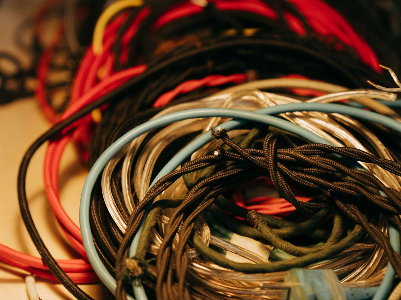 Rolos de fios e cabos elétricos em várias cores, vermelho, azul-claro e preto, sobre uma bancada